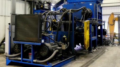Blue industrial baling machine with hydraulic hoses, cooling radiator, and electric motor on a factory floor